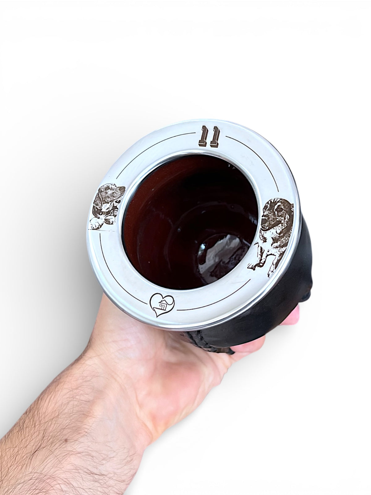 Mano sosteniendo un mate negro con dos perros grabados en la virola y un corazon con un mate